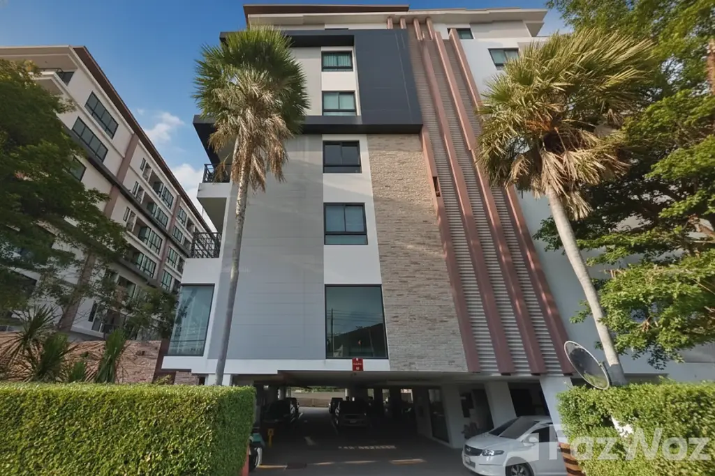 De Blue Condo exterior, a modern multi-story building with palm trees, hedges, and ground-level parking in Pattaya, Thailand.