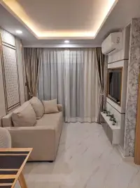 1 Bedroom Condo for Sale at Dusit Grand Park 2 living room with beige sofa, sheer curtains and wall-mounted TV