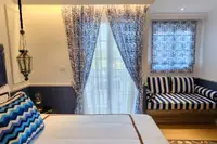 Studio Condo for Sale at Seven Seas Cote d'Azur: Bedroom with bed, striped sofa, and balcony doors with patterned curtains.