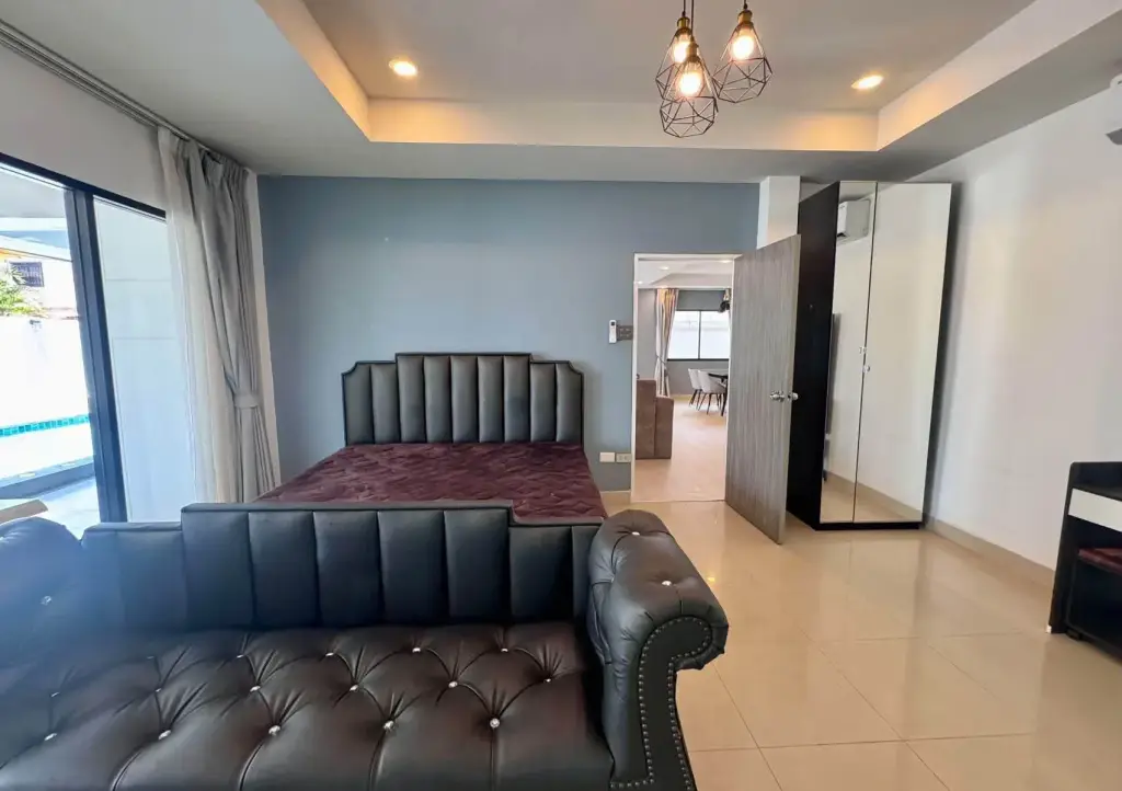 4 Bedroom House for Rent at Eakmongkol Village Chaiyapruek bedroom with black leather bed, sofa, and pool view through sliding doors