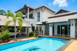 Baan Samran: Exterior view of the property with a swimming pool featuring a dolphin mosaic, covered carport, and lush greenery.