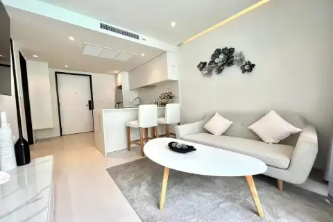 1 Bedroom Condo for Sale at Celine Wongamat bright living room with grey sofa, oval coffee table, and white kitchen bar counter