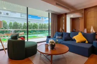Gardenia Pattaya living room with blue sofa, green armchair, wooden coffee table, and large window overlooking a garden.