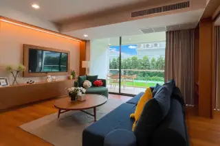 Gardenia Pattaya living room with blue sectional sofa, wooden coffee table, and a green armchair facing a large TV.