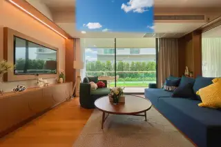 Gardenia Pattaya living room with a large wall-mounted TV, wooden console, blue sofa, and a view of the garden.
