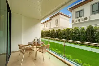 Gardenia Pattaya balcony with a small round table, two chairs, and a view of the green lawn and neighboring houses.
