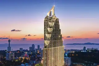 Grand Solaire Pattaya tall, modern skyscraper illuminated at dusk, with city lights, green spaces, and ocean in background.