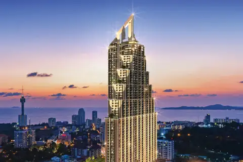 Grand Solaire Pattaya tall, modern skyscraper illuminated at dusk, with city lights, green spaces, and ocean in background.