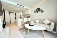 1 Bedroom Condo for Sale at Celine Wongamat contemporary living room with grey sofa, oval coffee table, kitchen bar, and decorative wall art