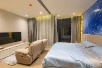 1 Bedroom Condo for Sale & Rent at Arom Wongamat wide-angle bedroom view with king bed, recliner sofa, TV unit, and blue feature wall
