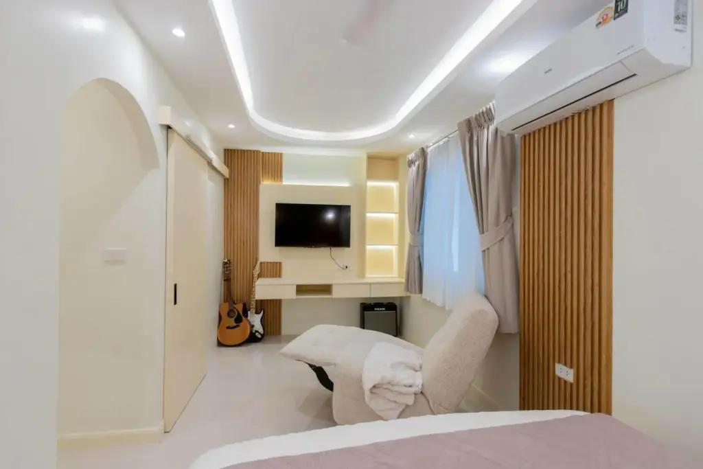 4 Bedroom House for Sale in East Pattaya bedroom with wall-mounted TV, wooden slat accents, and guitars