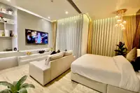 1 Bedroom Condo for Sale & Rent at Arom Wongamat: Modern bedroom with large bed, sofa, wall-mounted TV, and sheer curtains.