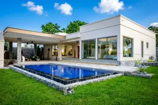 The Plantation Estates modern exterior with sliding glass doors revealing a luxurious bedroom, and a paved patio with accent lighting.
