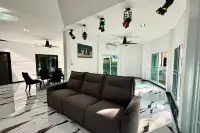 3 Bedroom House for Sale in Nong Prue living room with a brown reclining sofa, white walls, and black and white floor tiles.