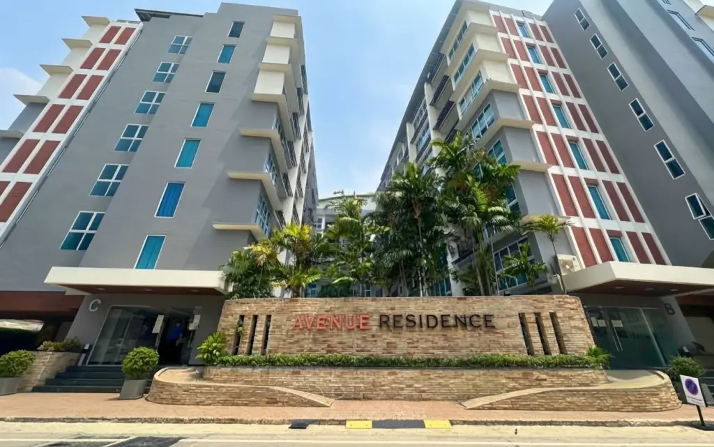 Avenue Residence modern condo buildings exterior with a stone sign displaying the property name and lush palm trees.
