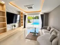 5 Bedroom House for Sale & Rent in Jomtien bright living area with sofa, TV, and sliding glass doors to pool