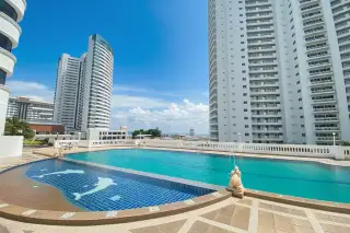 Jomtien Complex: Outdoor swimming pool with a covered seating area and white columns between two condo buildings.