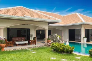 Jomtien Park Villas exterior with private pool, covered patio with wooden furniture, and manicured lawn.