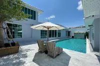 10 Bedroom House for Sale in Na Chom Thian: Swimming pool area with lounge chairs, umbrella, and modern light gray buildings.