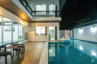 Baan Piam Mongkhon 3 modern house exterior at night with illuminated windows and a private swimming pool.