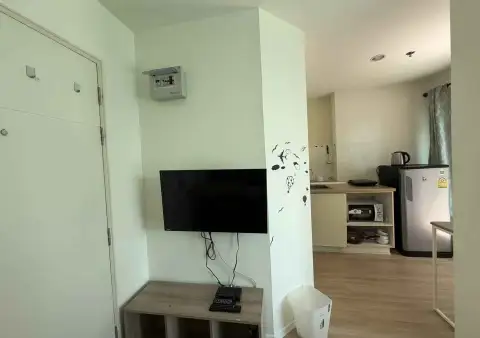 1 Bedroom Condo for Sale at Lumpini Seaview Jomtien living area with wall-mounted TV and kitchenette in background