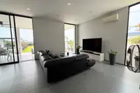 3 Bedroom House for Sale at The Prestige at Siam Royal View: Spacious living room with a black leather sofa, TV, and large sliding glass doors.
