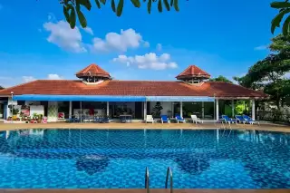 Chokchai Village 4 large outdoor swimming pool with blue tiles and a clubhouse building with a red roof.