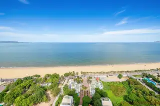 Metro Jomtien Condotel panoramic aerial view of the long sandy beach, ocean, and coastal road.