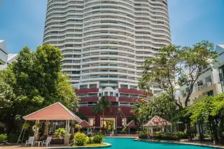 Metro Jomtien Condotel exterior of the building with red accents, surrounded by palm trees and a pool area.