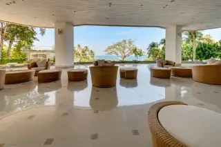 The Cove Pattaya outdoor lounge area with woven furniture and a view of the ocean and palm trees.