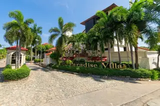 Paradise Villa 1 & 2 large cream house with red tile roof, multiple balconies, lush green garden, and elevated walkway.