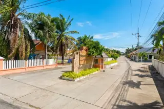 Srisuk Villa entrance gate with stone sign, palm trees, and residential road under a blue sky in Pattaya, Thailand.