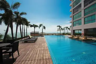Northshore Pattaya outdoor swimming pool with ocean view, wooden deck, and palm trees under a blue sky.