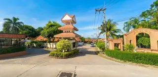 Baan Anda illuminated entrance with wooden doors, wall lanterns, and a swimming pool at dusk.