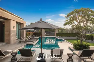 Patta Prime swimming pool area with sun loungers, umbrellas, and lush landscaping at sunset.