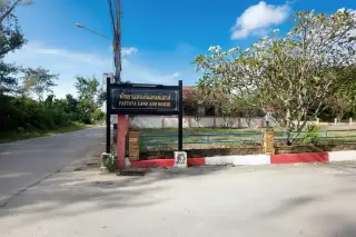 Pattaya Land And House entrance sign with black frame, red and white curb, and a paved road leading to the property.