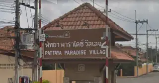 Pattaya Paradise Village 2 entrance gate from a wider street view with traffic and palm trees.