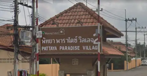 Pattaya Paradise Village 2 entrance gate from a wider street view with traffic and palm trees.