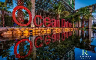 Riviera Ocean Drive large red 'Ocean Drive' sign reflected in a decorative water feature with palm trees and modern architecture.