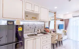 The Empire Tower Pattaya, a modern, compact kitchen with white cabinets, a small refrigerator, and a dining nook.