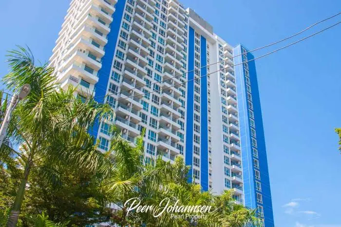 The Cliff tall white and blue modern condo building with many balconies and palm trees in the foreground against a blue sky.
