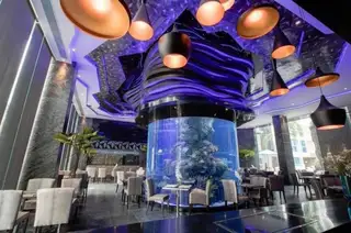 Centara Avenue Residence and Suites restaurant interior with a large cylindrical aquarium and purple ambient lighting at night.