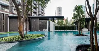 Baan Plai Haad large outdoor swimming pool with trees, modern building entrance, and city skyline.