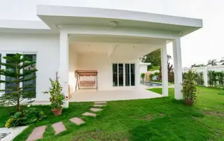Mountain Village 1 modern white house exterior with covered patio, swing chair, green lawn, stepping stones, and a swimming pool.