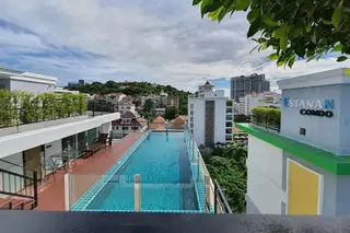 Estanan Condo: Rooftop infinity pool with city views, lounge chairs on a wooden deck, and the building's name sign.