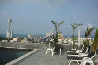 Tropicana Pratumnak rooftop pool deck with lounge chairs, umbrella, city skyline, Pattaya Park Tower, and ocean view.