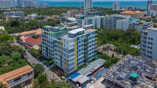Estanan Condo: Aerial view of the condo building in Pattaya, surrounded by other buildings and green spaces, with the ocean in the background.