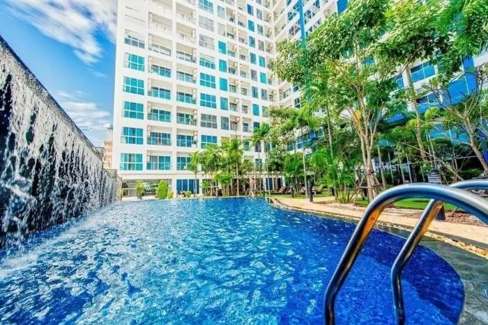 Nam Talay large outdoor swimming pool with waterfall feature, surrounded by lush palm trees and a modern white high-rise building.