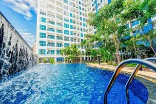 Nam Talay large outdoor swimming pool with waterfall feature, surrounded by lush palm trees and a modern white high-rise building.