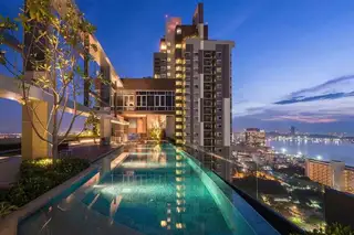 Centric Sea rooftop infinity pool with submerged lounge chairs and city skyline view at sunset.